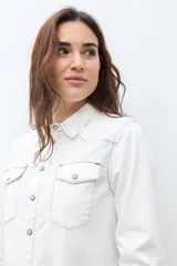 Camisa de jean color crudo, estilo western, con cuello y dos bolsillos frontales con tapa y botón. Presenta costuras contrastantes en tono rojizo.