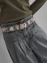Cinturón de cuero sintético con estampado animal print de vaca en tonos marrones y blancos. Hebilla metálica plateada con logo grabado.