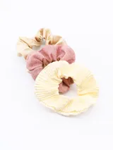 Set de tres scrunchies para el pelo, uno color beige satinado, uno rosa con glitter y uno amarillo claro plisado.