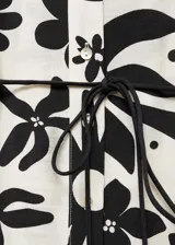 Blusa blanca con estampado floral negro, de tejido fluido, cuello de tira y cierre de lazo.