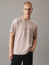 Remera color beige de corte regular, cuello redondo y mangas cortas. Presenta un monograma de Calvin Klein Jeans estampado en el pecho en color rojo y blanco.