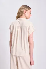 Camisa color crudo de lino, con cuello clásico, manga corta con dobladillo y cierre frontal con botones negros.