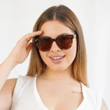 Lentes de sol negros con montura cuadrada y detalles metálicos dorados en las esquinas.