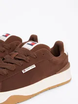 Zapatillas Tommy Jeans de corte bajo, color marrón, confeccionadas en gamuza con interior de poliéster y suela de goma. Presentan cordones, entresuela texturizada, etiqueta de la marca en el lateral y parche en la lengüeta.