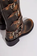 Botas de cuero gastado color marrón con hebillas y apliques de metal de caña alta.