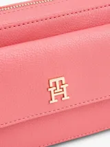 Bandolera Tommy Hilfiger color rosa con logo dorado en el frente y correa de tela a rayas.