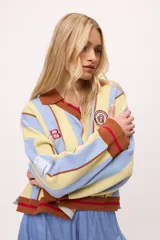 Sweater de punto color crudo con rayas verticales rojas, cuello polo marrón con borde negro, puños y ruedo acanalados en marrón y negro.