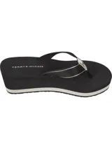 Ojotas de mujer con plataforma tipo cuña de color negro. Las tiras son de textil negro con una cinta decorativa que lleva el texto "HILFIGER" y el logo de Tommy Hilfiger en blanco y dorado. La plantilla lleva el logo de Tommy Hilfiger impreso.