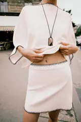 Minifalda blanca de tiro alto con cintura elástica y detalle de bordados negros en el ruedo y la cintura.