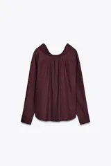 Camisa color borgoña de Zara Woman Collection, confeccionada en algodón popelín. Tiene cuello solapa, escote en pico, mangas largas con puños abotonados, bajo redondeado y cierre frontal con botones.