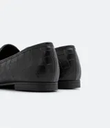 Mocasines negros con textura croco, puntera redondeada y detalle metálico en la parte superior.