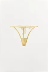 Tanga color dorado semitransparente con detalle de encaje floral en el frente. Cintura elástica fina y ajustable.