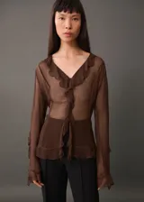 Blusa marrón de gasa semitransparente con escote en V y volantes. Tiene corte recto y mangas largas.
