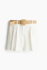 Short blanco de sarga con cinturón ancho extraíble de rafia con hebilla cuadrada con detalle de perlas. Modelo de corte holgado con tiro alto, bolsillos laterales discretos, bolsillos atrás insertados y cierre con botón y corchete ocultos. Piernas con pinzas y pliegues adelante y atrás.
