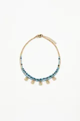 Collar doble con cuentas de vidrio azules y negras, y dijes colgantes dorados con diseño de anclas.