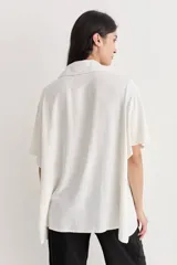 Camisa color crudo de corte amplio con bordados florales negros en la parte superior. Tiene cuello camisero, mangas cortas y cierre frontal con botones negros.