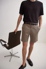 Short color marrón claro, de corte recto y largo a la rodilla. Presenta cintura con elástico en los laterales, cierre con botón, bolsillos al bies y bolsillos traseros ribeteados con botón.