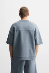 Sudadera negra de corte relaxed fit, confeccionada en tejido interlock de algodón con elasticidad. Tiene cuello redondo, manga corta y bajo acabado en rib.