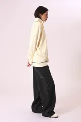 Buzo color crema con cuello alto con botones y ribete negro en cuello, puños y ruedo.