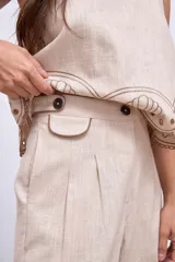 Pantalón de lino color beige con bordados de palmeras y conchas marinas en color marrón.