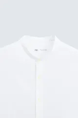 Camisa de algodón blanco con efecto arrugado, cuello mao (tira) y manga larga con puño abotonado. Presenta un corte relajado (relaxed fit) y cierre frontal de botonadura.