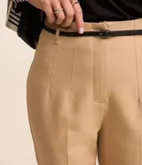 Pantalón de vestir azul marino, de corte zanahoria, con cinturón fino negro con hebilla dorada.