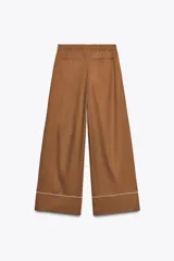 Pantalón marrón de popelina con corte palazzo, tiro medio, cintura elástica ajustable con cordones, bolsillos laterales y falsos bolsillos de vivo con botones en la espalda. Detalle de vivos blancos a contraste en el ruedo.