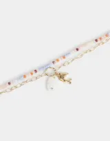 Pulsera multicadena con una cadena de mostacillas de colores y otra dorada de eslabones. Incluye dijes colgantes: un corazón de nácar y un delfín dorado.