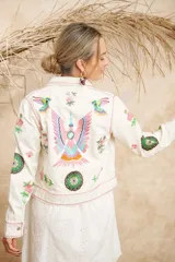 Campera color crema de algodón con estampado de flores, plumas y colibríes, con cuello camisero, cierre frontal con botones metálicos y mangas largas.