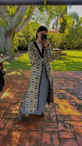 Vestido tipo abrigo con estampado geométrico en tonos azul, marrón y verde, con cuello en V, mangas abullonadas y cierre frontal con botones.