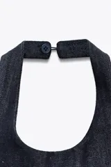 Top de cuello halter confeccionado en tejido denim azul. Detalle de pespuntes marcados a tono y espalda descubierta.