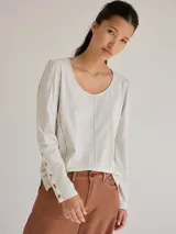 Remera blanca de algodón con escote redondo, mangas largas y pespuntes verticales a contratono.