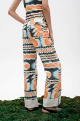 Pantalón de jean azul oscuro con corte acampanado, tiro medio y dobladillo en el ruedo. Presenta costuras marcadas en el frente y estampado abstracto en tonos grises y blancos en el interior del dobladillo.