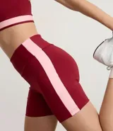 Bermuda deportiva femenina color bordó, tiro alto, confeccionada en microfibra. Presenta un recorte lateral contrastante de color rosado claro que recorre la pierna.