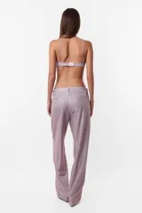 Pantalón de tela glitter color lila, de corte sastrero clásico y tiro medio. Tiene pasacinto, cierre con gancho metálico y cierre en cartera, bolsillos laterales diagonales y bolsillos traseros ribete falsos.