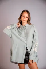 Camisa celeste de corte clásico, con botones frontales y bordados florales en las mangas.