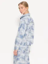 Chaqueta corta de algodón con estampado tie-dye en tonos celeste y blanco. Tiene cuello camisero, cierre con botones metálicos, bolsillos plaqué en el frente y remaches con brillos en el canesú de la espalda.