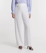 Pantalón blanco de crepé, corte recto, con trabillas en la cintura, cierre con botón y cremallera, y colgante de corazón metálico.