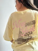 Remera amarilla de corte holgado con estampado de Nueva York en tonos rosa y marrón.