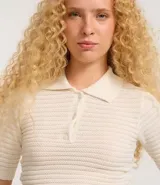 Blusa de punto color crema, con cuello polo, mangas cortas y puños con botones.