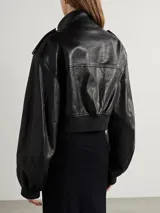 Campera bomber corta de cuero sintético negro, con cuello alto, cierre frontal, hombreras con botones a presión y bolsillos con solapa y botón a presión.