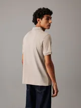 Chomba Calvin Klein color beige con cuello polo y media cremallera. Tiene mangas cortas y un parche de goma con el logo de la marca.