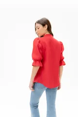 Blusa de lino color rojo con volados frontales que enmarcan el pecho, cuello redondo con mini volado y mangas 3/4 abullonadas con puño elástico. Presenta un cierre frontal con botones y una silueta relajada.