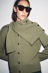 Chaqueta de punto color rosa pálido, con cuello redondo y cierre frontal de botones oscuros. Presenta mangas largas y un corte a la cintura.