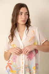 Camisa de seda blanca con bordados florales multicolores, cuello camisero, manga corta y cierre frontal con botones forrados.