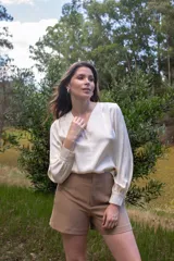 Blusa color crema con escote en V y mangas largas con puños abotonados.