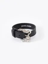 Pulsera de cuero vacuno negro con diseño regulable, marca Jazmín Chebar. Presenta un cierre de hebilla metálica plateada con forma de dragón.