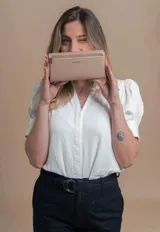 Billetera color beige con doble compartimento con cierre, correa de mano y logo de la marca en el frente.