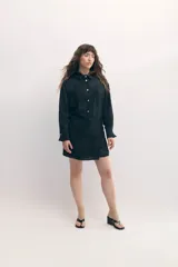 Vestido camisero negro con sobrefalda integrada, botones de nácar y estampado con leve rugosidad.