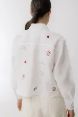 Camisa azul de lino con cuello clásico, manga larga y cierre frontal con botones. Presenta bordados de dados, cartas y el nombre de la marca.